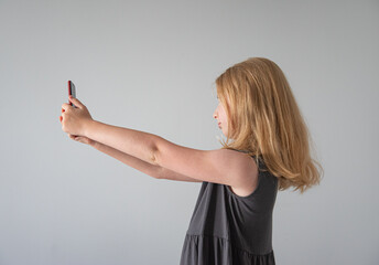 girl in gray dress  and with a  phone on the gray background  takes selfie