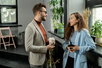Two young smiling colleagues having discussion at break in office