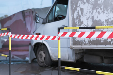 White lorry collided with a glass wall of shopping mall. Road accident site isolated and fenced off with signal tape.