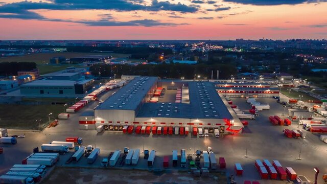 Hyper lapse (hyperlapse - motion time lapse) of a logistics park with a loading hub. Semi-trailer trucks standing at warehouse ramps for loading and unloading goods at dusk. Aerial panoramic view