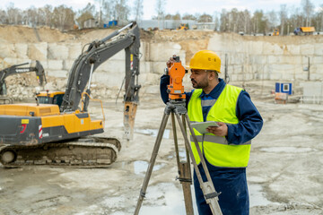 Surveyor in uniform standing by total station against bulldozer at construction site
