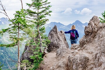 Back view of a blond woman traveler standing between rocks in the mountains. She admires the beautiful mountain views.