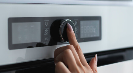 Female finger is touching the button of modern panel of electric oven. Technology concept. Focus to...