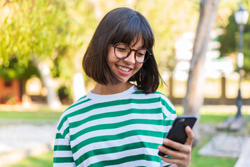 Young brunette woman in the park sending a message or email with the mobile