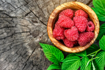 Fresh juicy raspberries in wooden bowl. Summer still life with raspberries on an old wooden table. Copy space .Jar of raspberry jam and fresh berries on wooden background