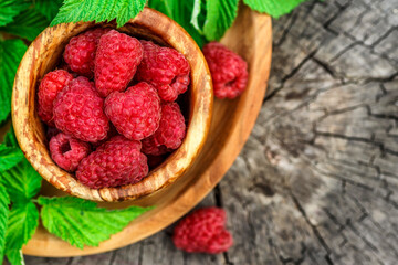 Fresh juicy raspberries in wooden bowl. Summer still life with raspberries on an old wooden table. Copy space .Jar of raspberry jam and fresh berries on wooden background