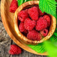 Fresh juicy raspberries in wooden bowl. Summer still life with raspberries on an old wooden table. Copy space .Jar of raspberry jam and fresh berries on wooden background