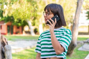 Young brunette woman in the park keeping a conversation with the mobile phone with someone