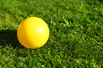 Round beautiful yellow rubber inflatable children ball lies on green fresh mowed lawn grass in light of summer sunset evening sun. Active games in country fresh air nature hot days