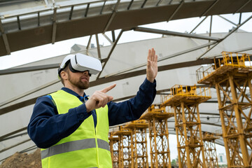 Young engineer in virtual reality glasses standing outdoors and gesturing, he working on online construction site