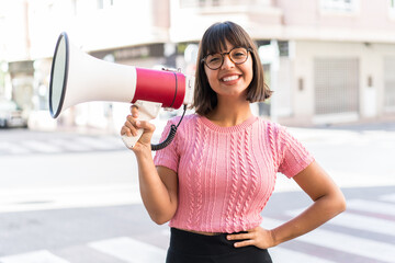 Young brunette woman in the city holding a megaphone and smiling
