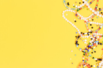 Necklaces and bracelets made from beads and pearls scattered on a yellow background with copyspace.