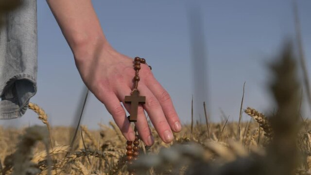 woman holding a christian cross walks in a wheat field