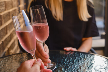 A glasses of rose wine in the hands of a girl and man who relaxing on restaurant terrace. Summer holiday. Celebrate and enjoy moment. Alcoholic drink tasting. Romantic evening aperitif