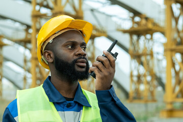 African construction worker in work helmet talking in transmitter while working on construction...