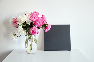 Black canvas mockup with pink flowers on table on white wall background