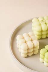 A pastel yellow bubble candle on a concrete tray on a beige colored background, close up