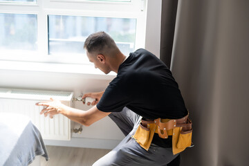 young man plumber checking radiator while installing heating system in apartment