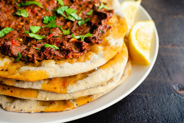 Closeup View of Turkish Lahmacun Served with Lemon Wedges: Turkish flatbreads topped with spiced ground meat and garnished with chopped mint leaves
