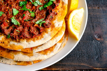 Closeup View of Turkish Lahmacun Served with Lemon Wedges: Turkish flatbreads topped with spiced ground meat and garnished with chopped mint leaves