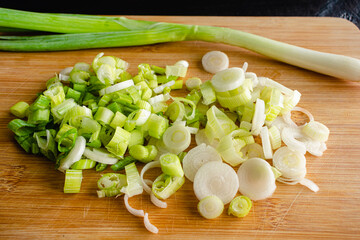 Closeup View of a Sliced Green Onion on a Bamboo Cutting Board: Slices of scallion on a wooden cutting board with a whole scallion in the background