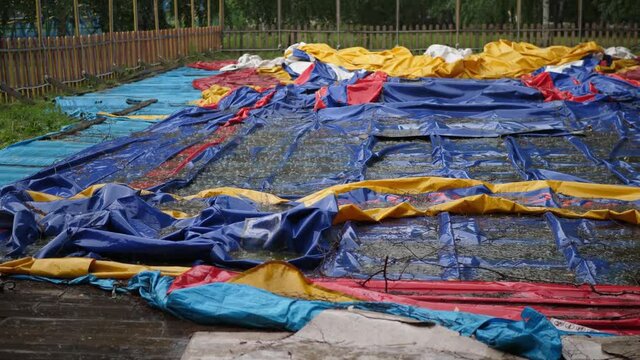 noisy blows of rain on a destroyed deflated inflatable house with muddy puddles in a public amusement park after a heavy downpour with an audio.