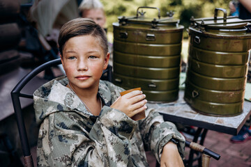 Boy in camouflage relax and drinks tea after playing in laser tag shooting game with a weapon outdoor
