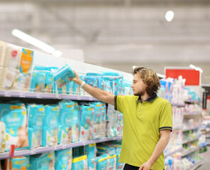 Man shopping in supermarket reading product information.(diapers,detergent)