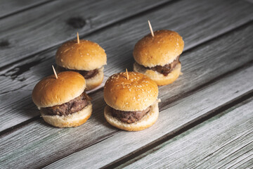 Mini beef hamburgers with smooth bread on a wooden surface