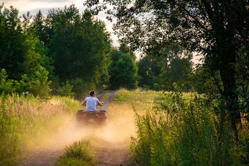 young man driving a quad bike down a dirt road at sunset © Remigiusz Góra