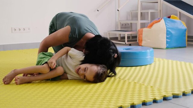 Mother playing with cute disabled child Talking, communicate with cerebral palsy boy on the floor mat, tickle at home Woman laughing with kid, physical or mental limits in movements. Fun