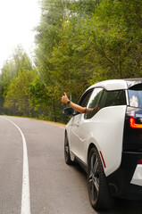 view of the side of the electric car at a bend in the road and the driver's hand shows ok