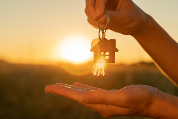 The hand holds the key to the new house with a keychain in the form of a house on the background of...