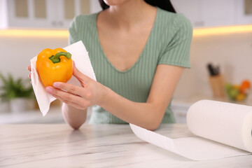 Woman wiping bell pepper with paper towel in kitchen, closeup