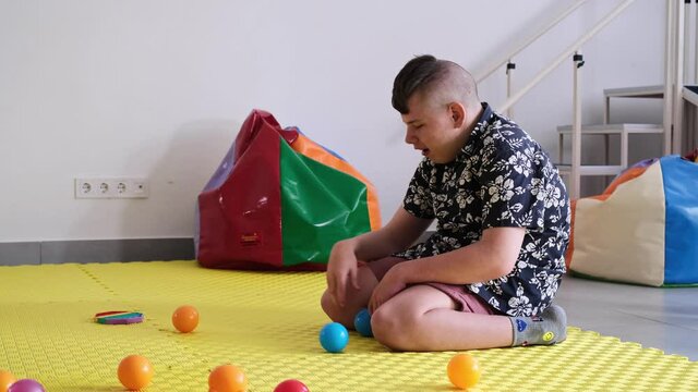 Children with disability getting sensory activity with toys, balls, small objects, cerebral palsy boy playing calming game, training fine motor skills. Rehabilitation center with therapist, mother