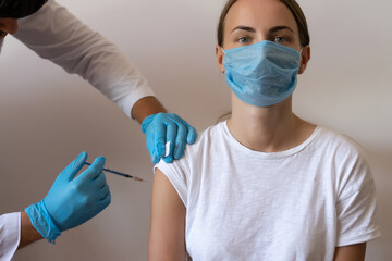 Woman and her doctor wearing face masks and getting a vaccine shot in a doctor's office. Doctor making injection to female patient in clinic