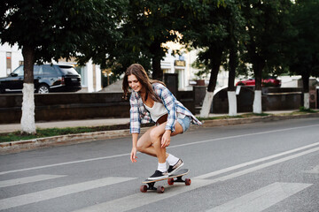 Carefree happy woman riding on a skateboard on an empty city road in low stance