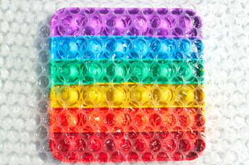 Bubble wrap film over a rainbow Pop It fidget toy