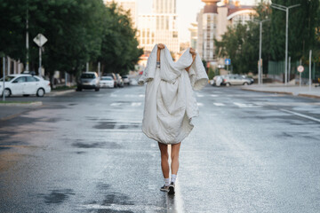 Bare legged woman wrapped in blanket walking down empty city road in the morning