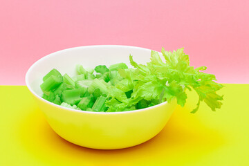 Fresh Chopped Celery Pieces with Water Drops in White Bowl on Yellow Background. Vegan and Vegetarian Culture. Raw Food. Healthy Diet with Negative Calorie Content
