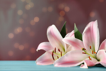 Beautiful pink lily flowers on turquoise table against blurred lights, space for text