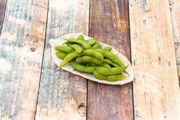 Small leaf shaped tray holding portion of Asian edamame in pod with some sea salt on wooden table