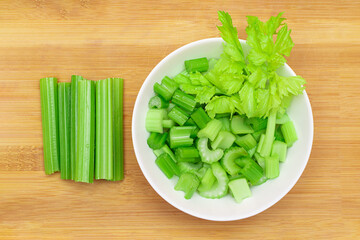 Fresh Chopped Celery Sticks with Water Drops in White Bowl on Bamboo Cutting Board - Top View....