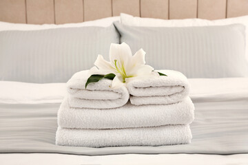 Obraz na płótnie Canvas Stack of fresh towels with flower on bed indoors