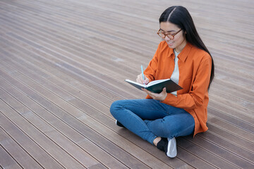 Beautiful smiling asian woman writing note, planning project sitting outdoors, copy space.  Happy university student studying, learning, education concept