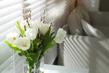 Beautiful bouquet of willow branches and tulips in vase near window indoors, space for text
