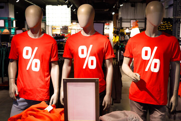 Three dummies in store shop mall in red t-shirts with percent symbol sign. Sales discounts concept. Small clean copyspace table