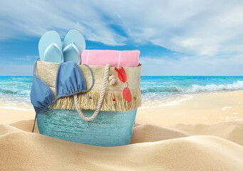 Stylish bag with different accessories on sandy beach near ocean