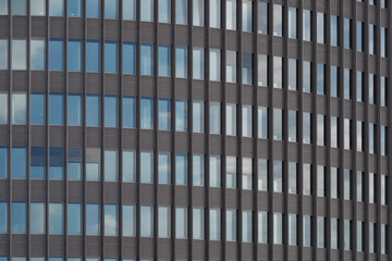 Typical modern facade with rectangular grid frame structure and reflection of  blue sky on reflective glass of high rise office building. 