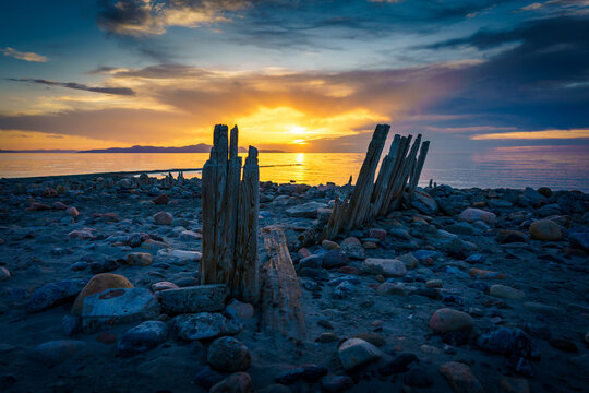 Sunset over the lake with a rocky beach and eroded pier wood - Powered by Adobe